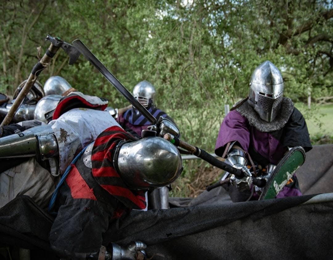 Four people in armour, the nearest leaning sideways while being hit with polearm